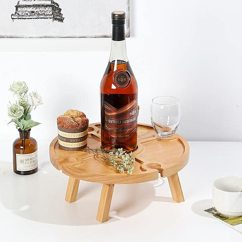 Wooden round wine rack picnic table holding a bottle, glasses, and appetizers on top