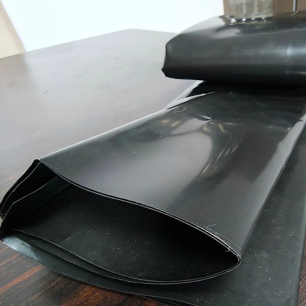 Rolled black pond liner sheet laid out with curved edge on installation surface