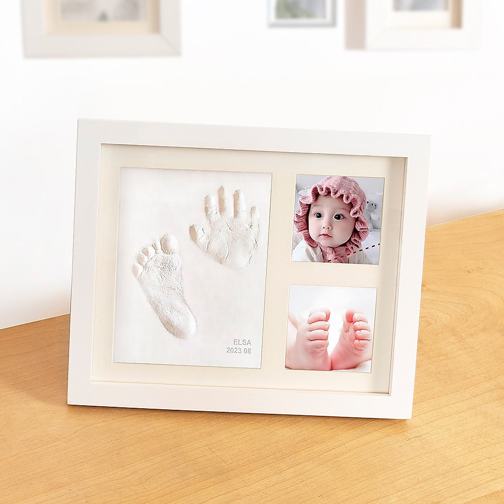 White photo frame displaying baby hand and foot clay prints with two small photos