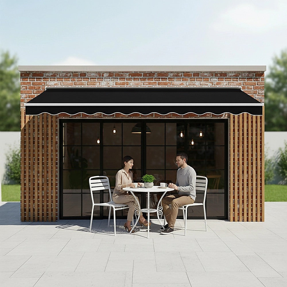 Black retractable awning canopy with scalloped valance over outdoor table and chairs