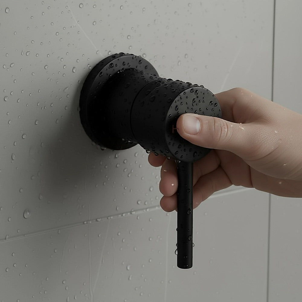 Matte black shower bath mixer tap being operated, with water droplets on surface