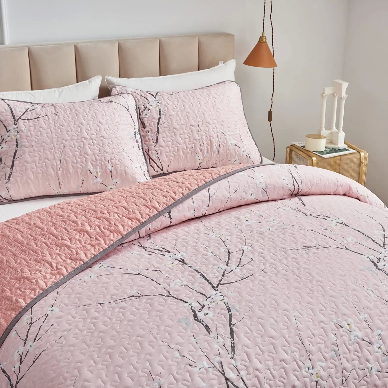 Quilted coverlet and pillowcases in light pink with branch floral pattern, close-up
