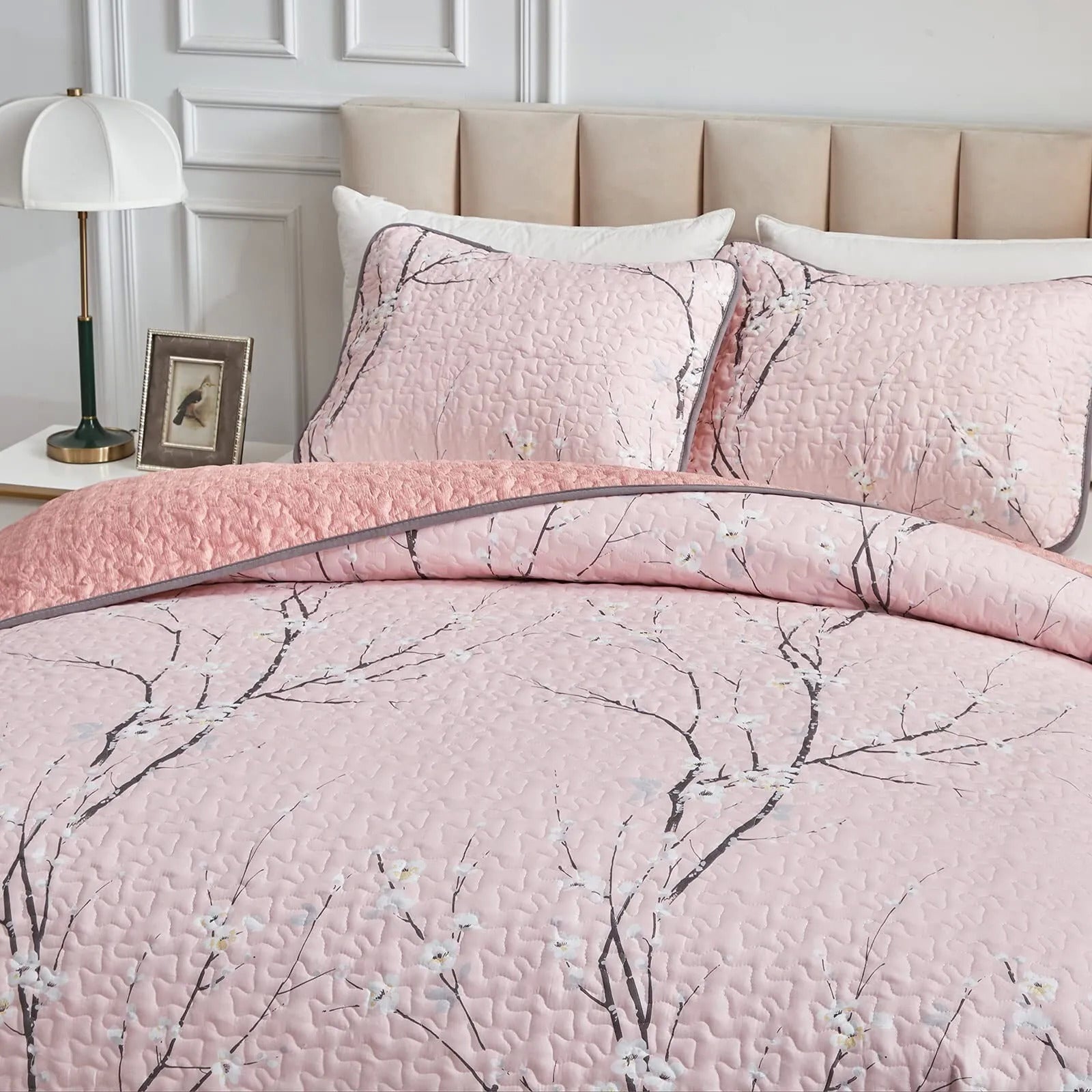 Quilted coverlet and pillowcases in light pink with branch floral pattern, corner view