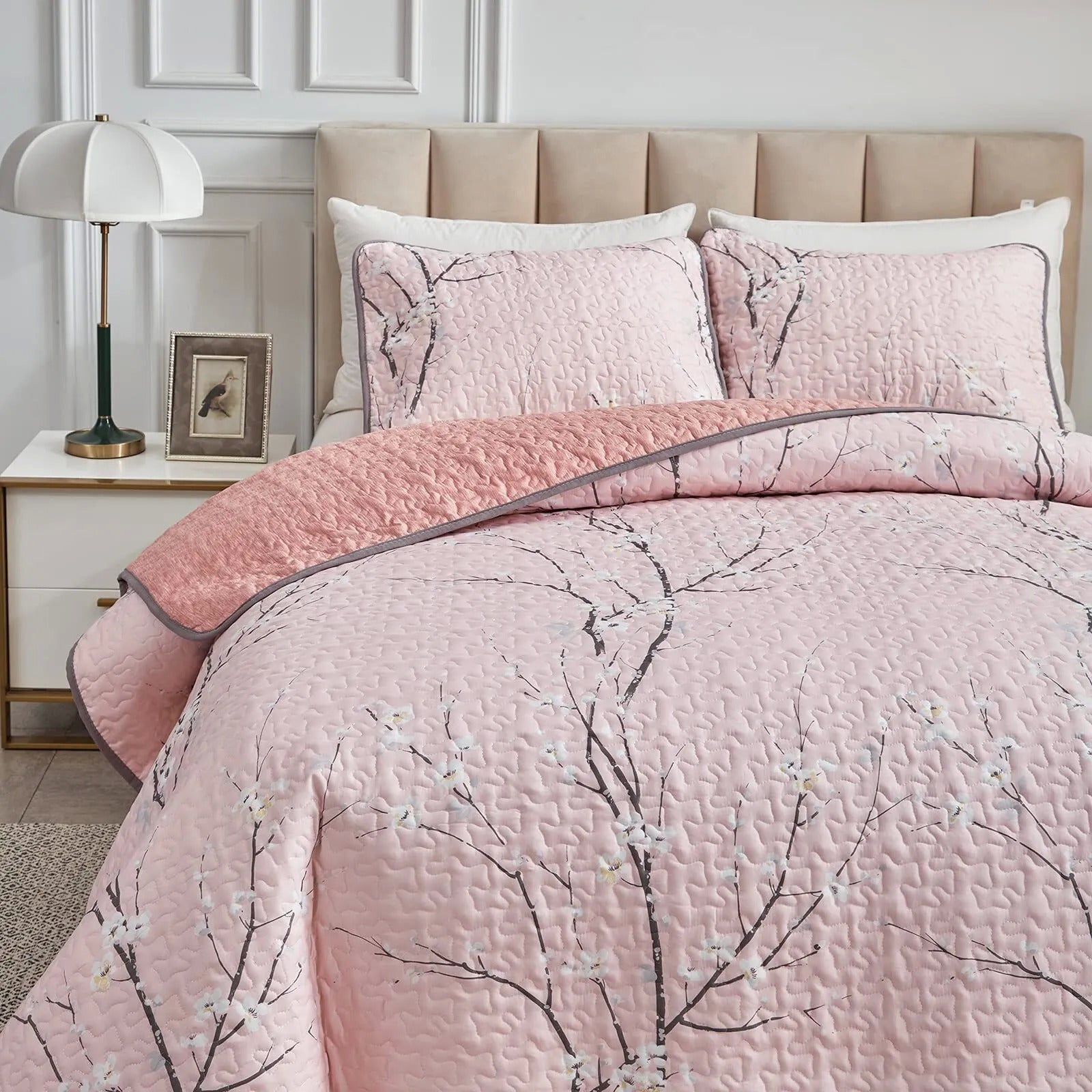 Quilted coverlet and pillowcases in light pink with branch floral pattern on bed