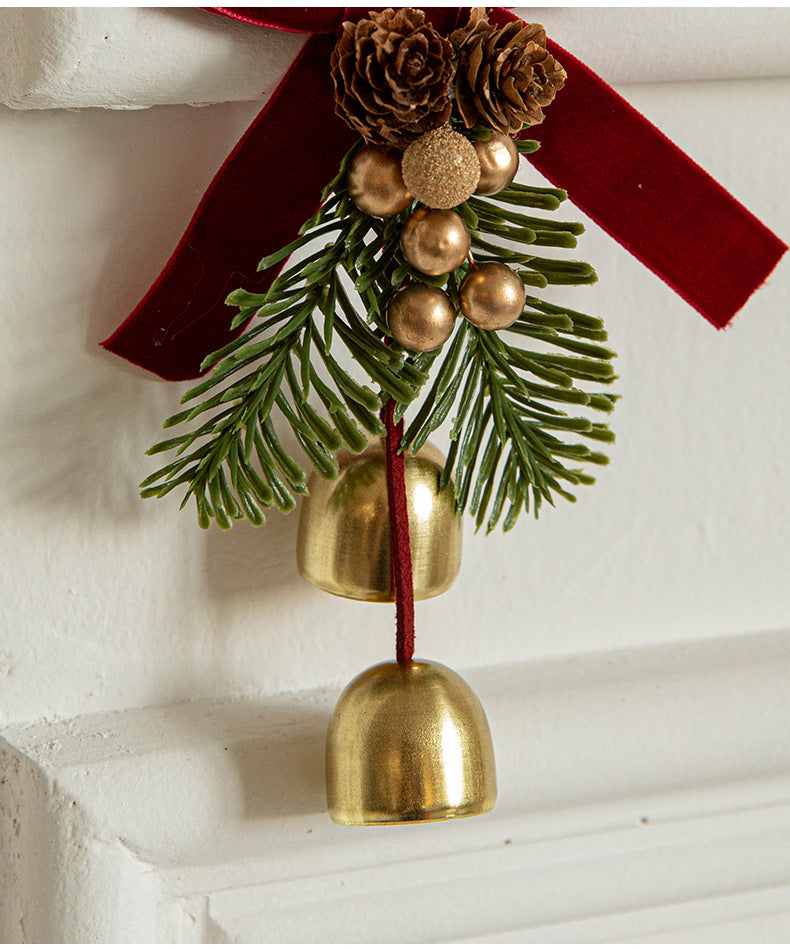 Hanging ornament close-up with red bow, pinecone cluster, evergreen sprigs, and gold bell