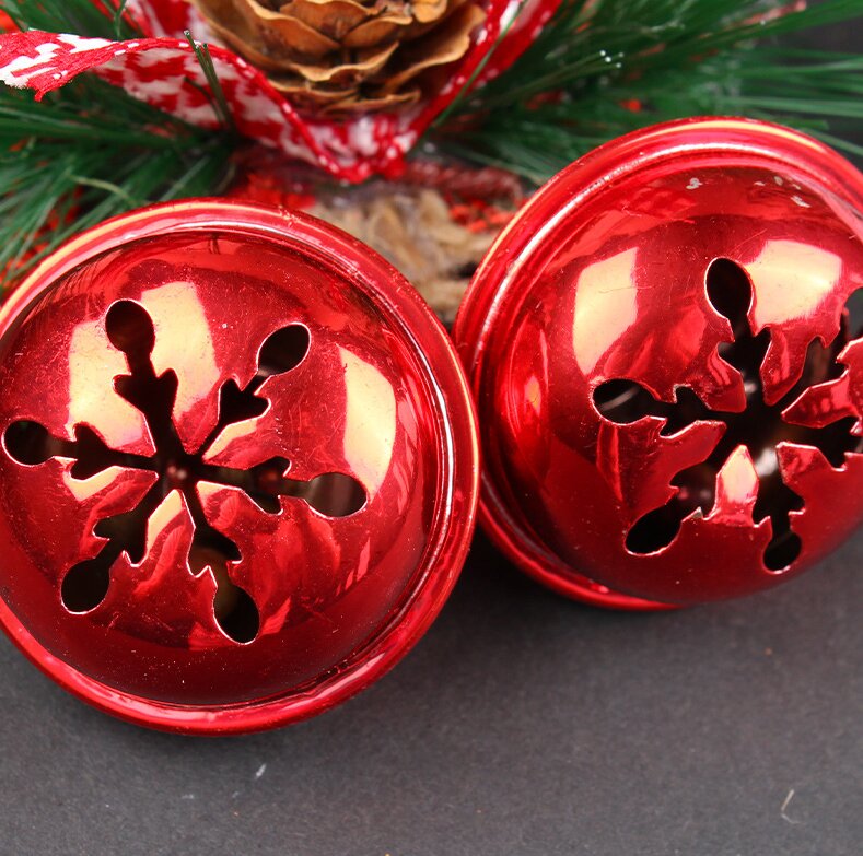 Red bell ornaments with snowflake cutouts, with pinecone and pine needles behind