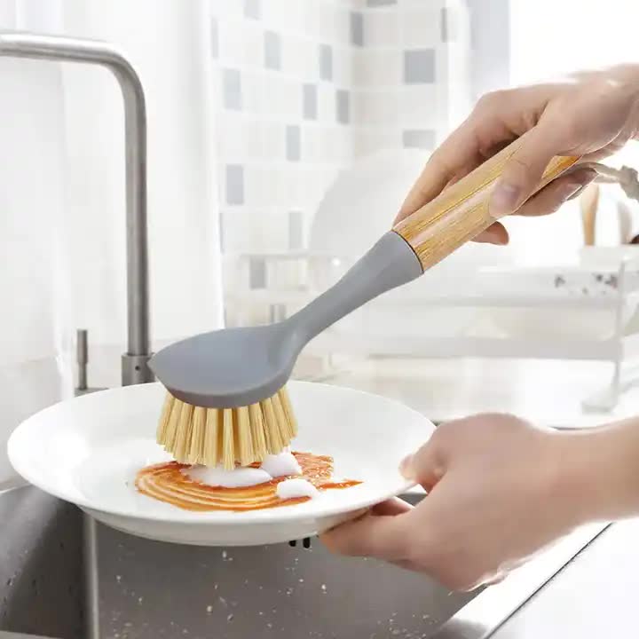 Dish scrub brush with gray head and yellow bristles, held over a plate