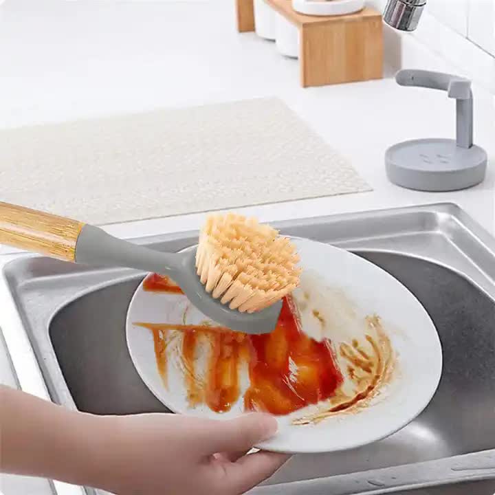 Dish scrub brush with gray head and tan bristle dome, scrubbing a plate