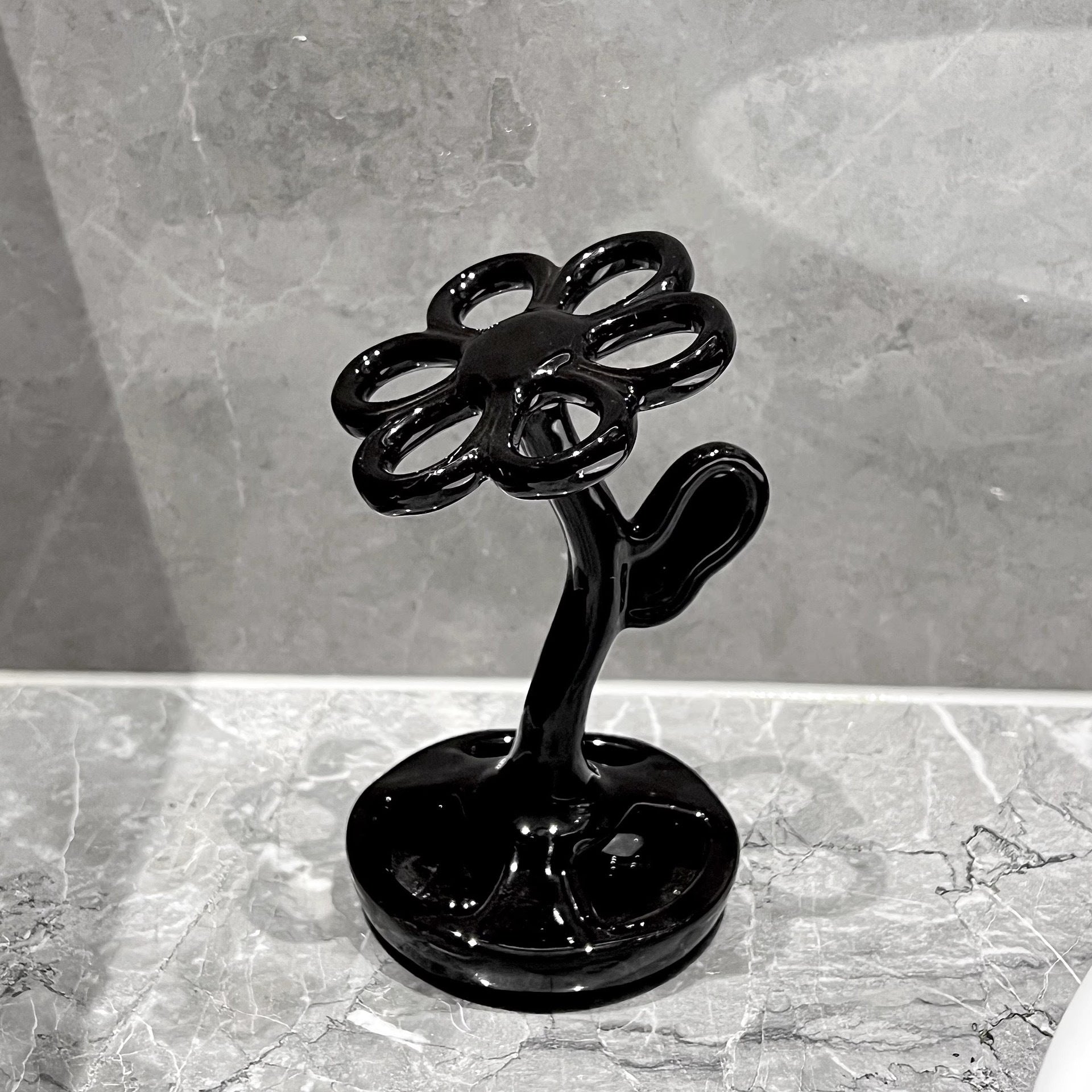Black ceramic flower toothbrush holder with arched stem and round base.