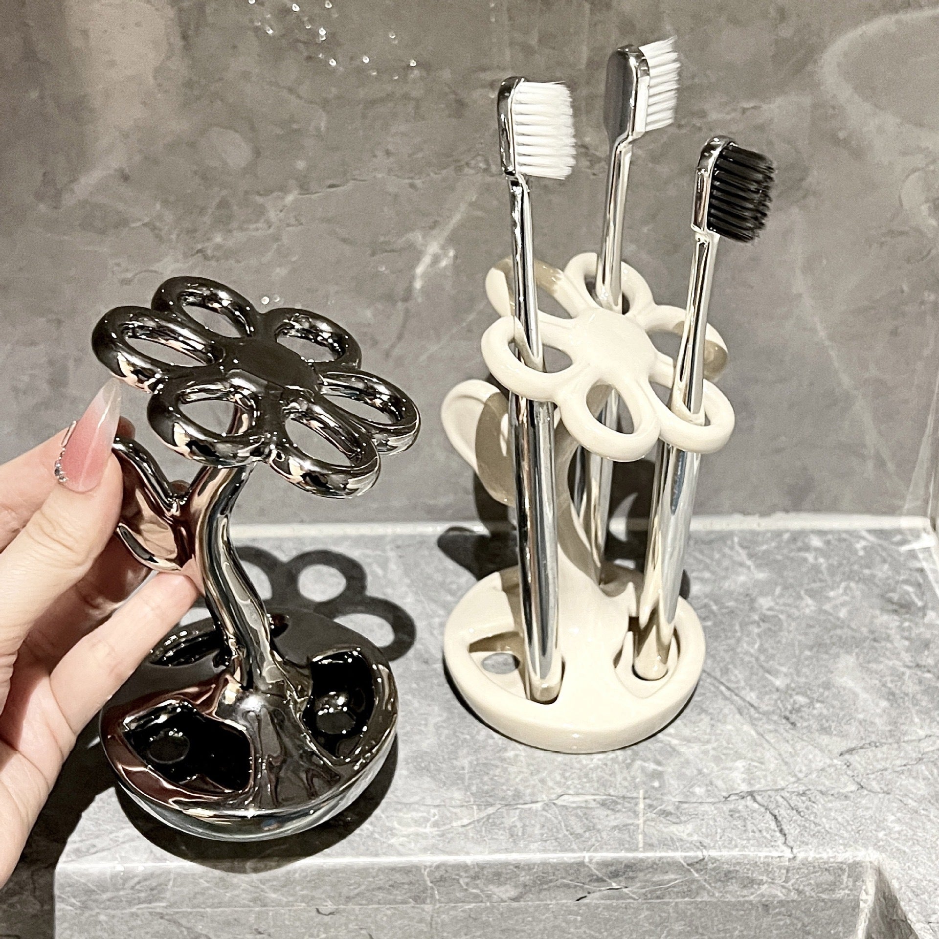 Black and milky white ceramic toothbrush holders, one held by hand beside brushes.
