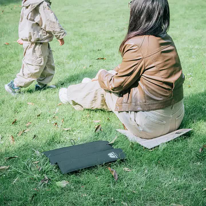 Outdoor foldable seat pad under seated person on grass, dark gray
