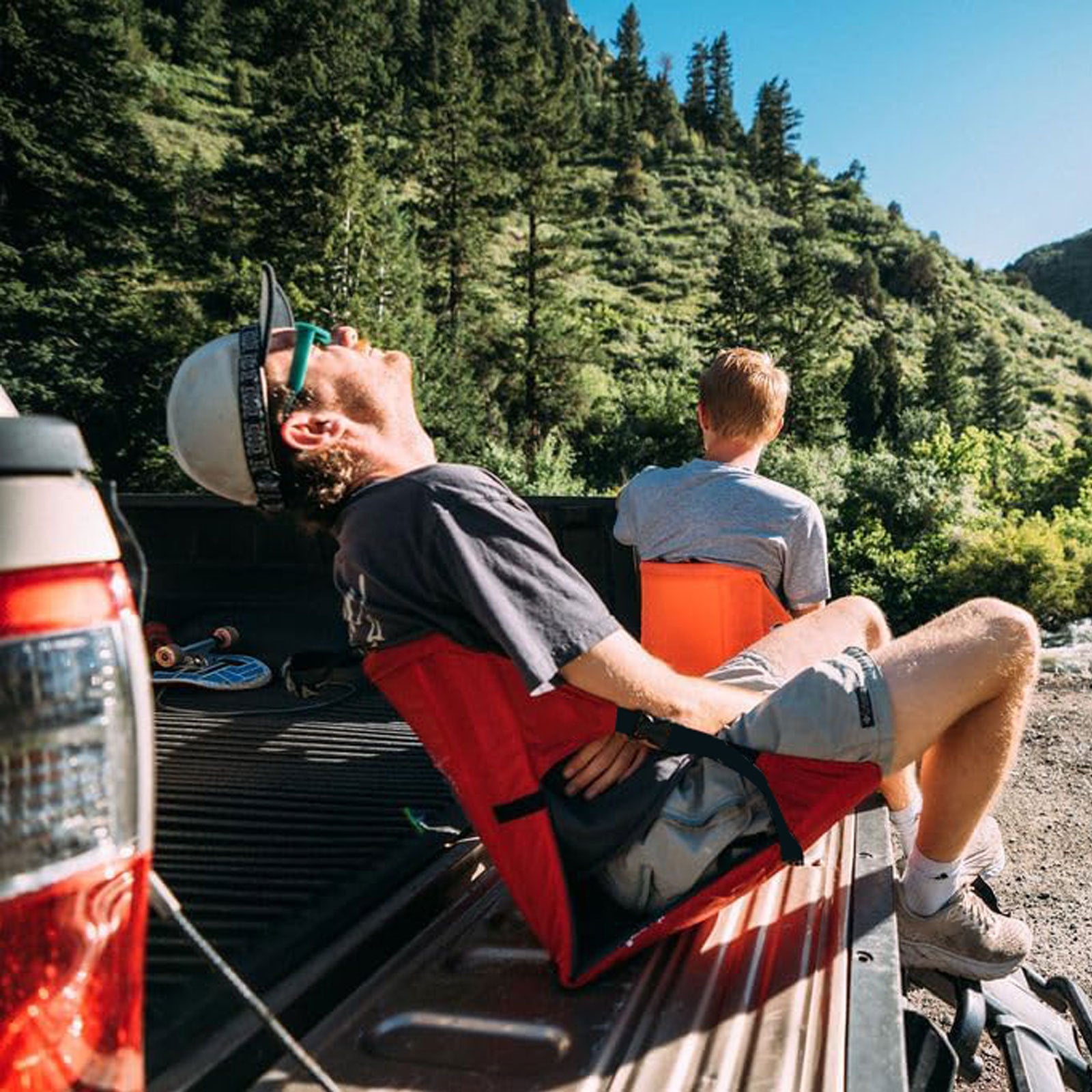 Red and black foldable camping seat pad with backrest and seat cushion, secured by straps.