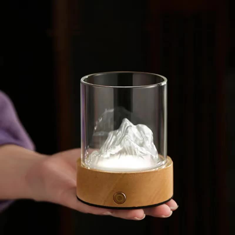 Glass mountain night light with white glow held in hand, clear cylinder and cork base