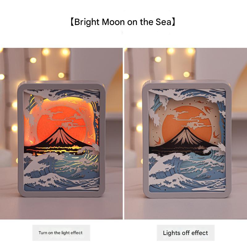 3D paper carving night light showing moon over sea, with light on and light off views