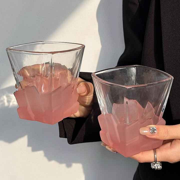 Pink frosted ice-cube textured glass tumbler with clear rim, held in hand