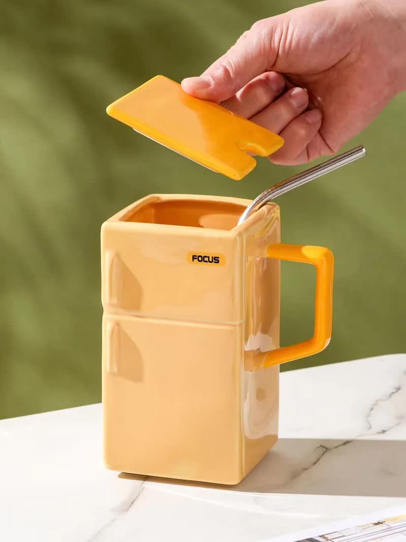 Yellow ceramic mug with flip lid and straw, side handle; lid held open by hand