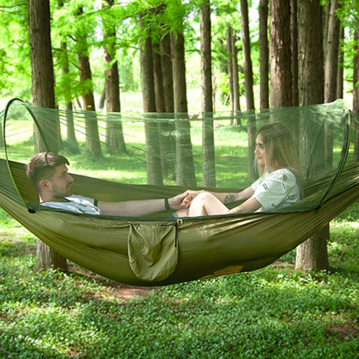 Mosquito net hammock hanging in a forest with two people resting inside