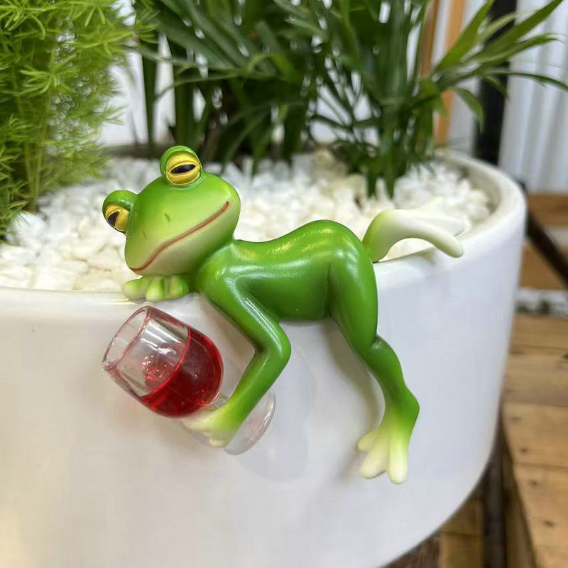 Green frog ornament lying beside a clear glass mug, for fish tank edge decor