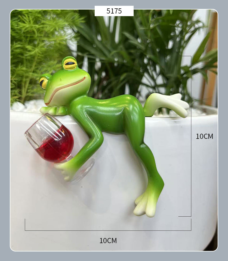 Green frog ornament lying on a tank edge with a red clear-glass mug