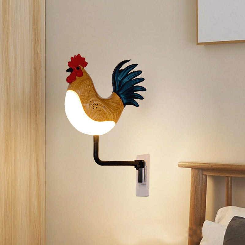 Rooster wall lamp on black arm with glowing bulb, red comb and blue tail, wall bracket