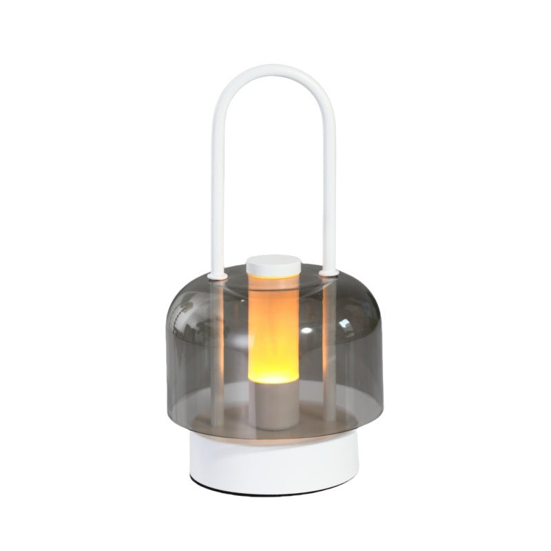 Portable LED lantern with clear smoky glass shade, lit warm glow, and white handle