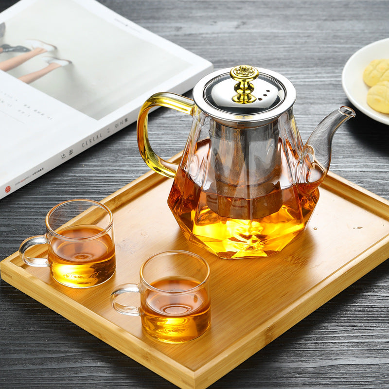Glass teapot with gold handle and stainless infuser, amber tea on a wooden tray