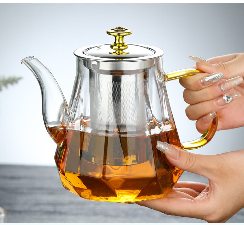 Glass teapot with gold handle and stainless lid, held in hands with amber tea