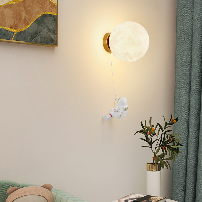 Moon wall lamp with glowing orb and gold wall mount, astronaut hanging by cord