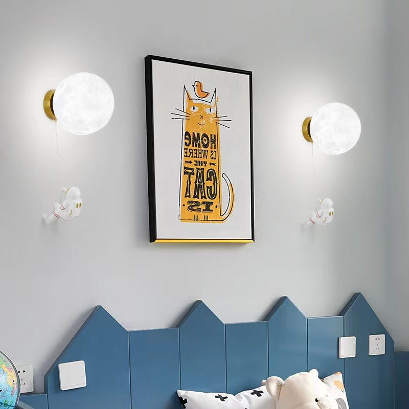 Two moon wall lamps with glowing orbs, gold mounts, and hanging astronaut figures
