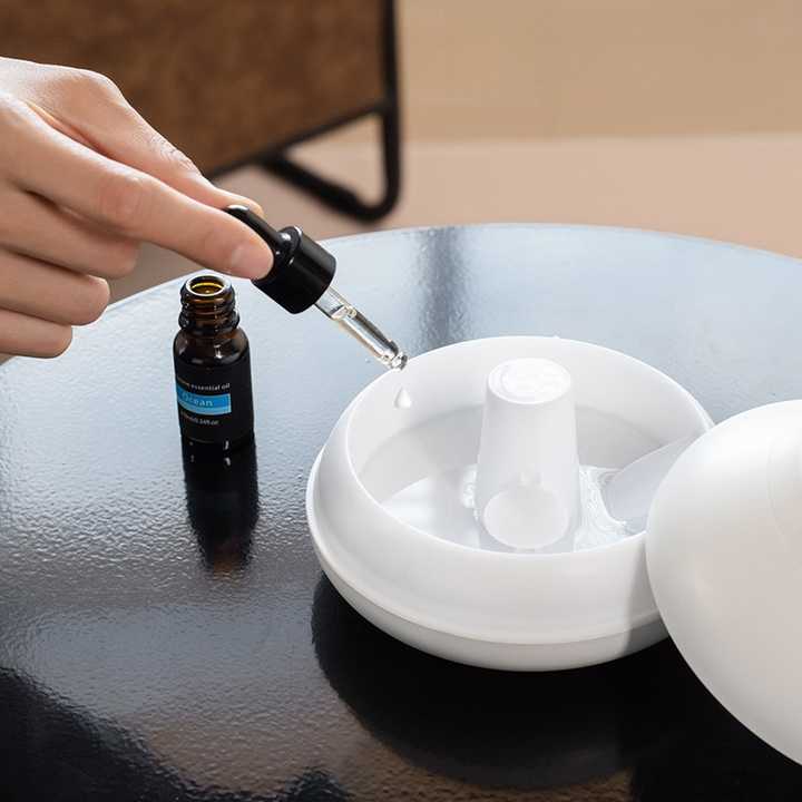 Hands adding oil to a white aroma diffuser with central column