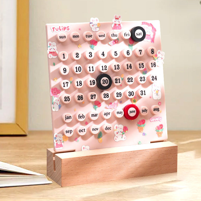 Pink perpetual desktop calendar with month labels and numbered ring discs on stand