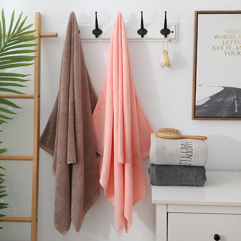 Pink bath towel hanging on wall, with embroidered 'Happy' text