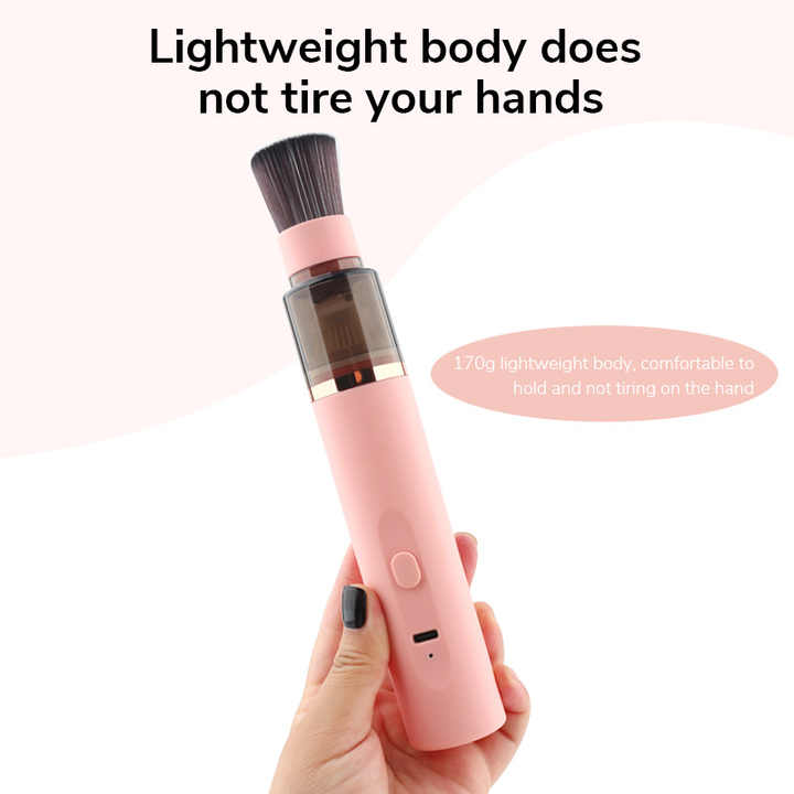 Pink handheld dust vacuum cleaner with soft brush head held in hand