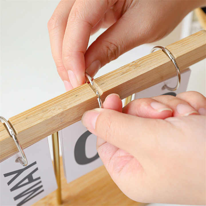 Desktop wooden flip calendar close-up, hands adjusting a wooden bar with metal clips