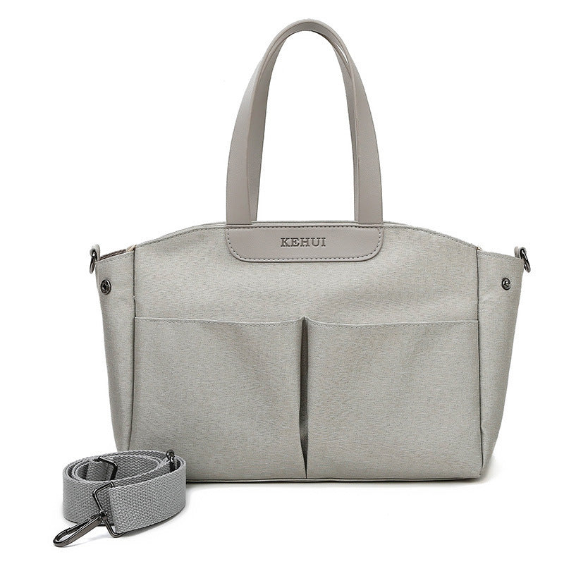 Grey diaper bag tote with top handles, front pockets, and detachable strap