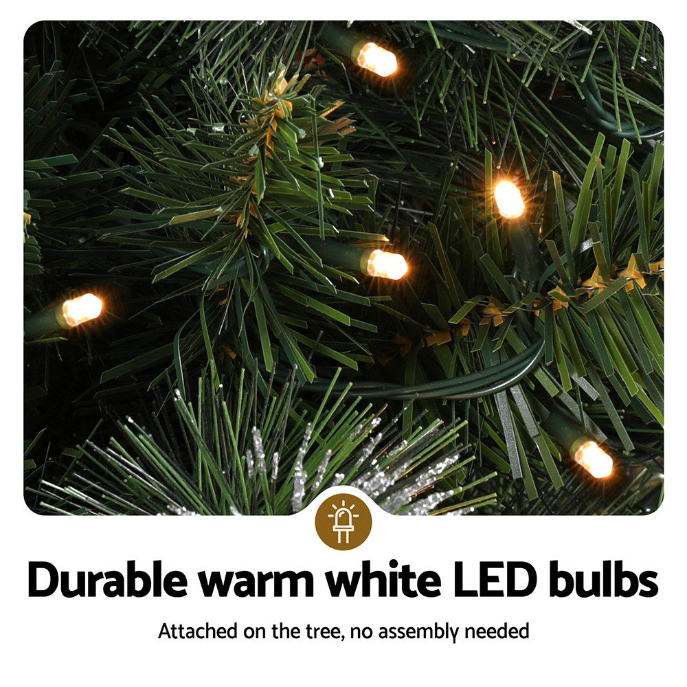 Glowing warm white LED bulbs on Christmas tree needles with silver glitter tips