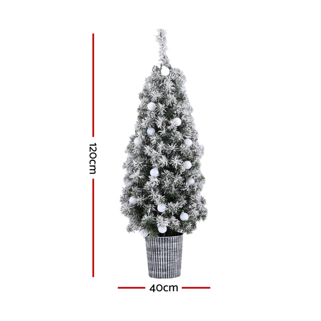 Slim potted snowy Christmas tree in a ribbed bucket with warm white globe lights