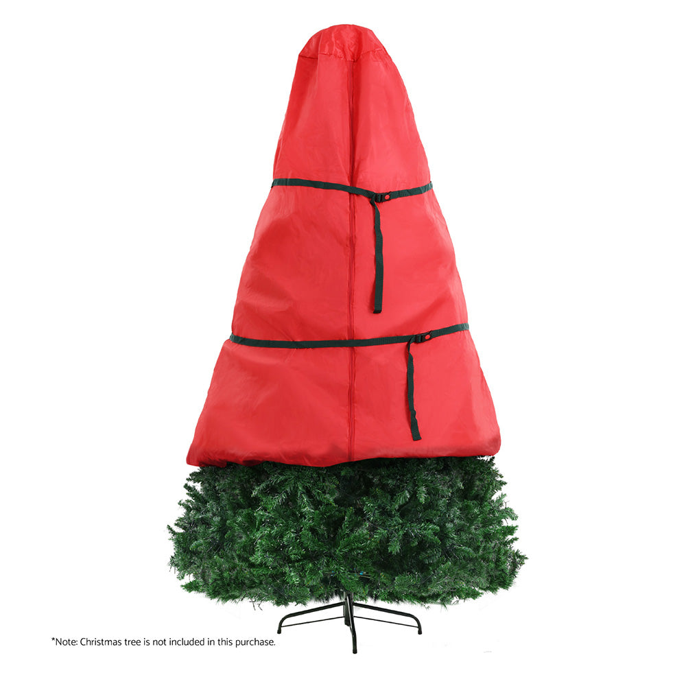 Red Christmas tree storage bag with black strap bands covering a green artificial tree.