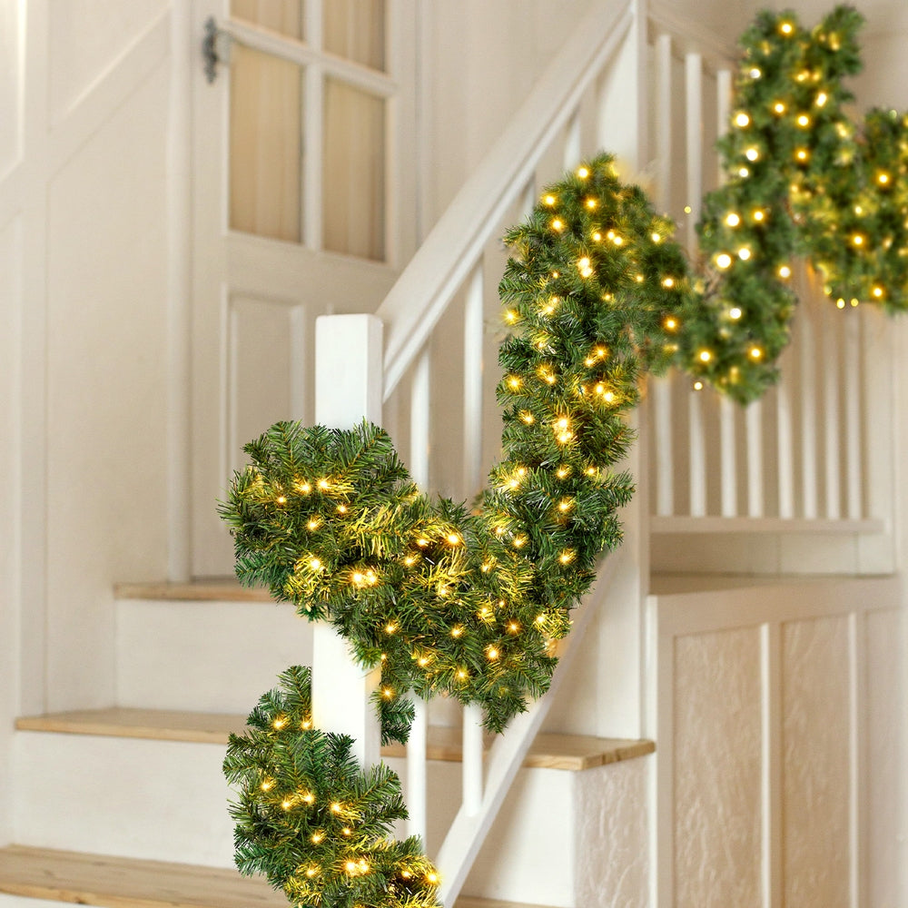 Pre-lit Christmas garland with warm yellow LEDs over a staircase banister, green foliage