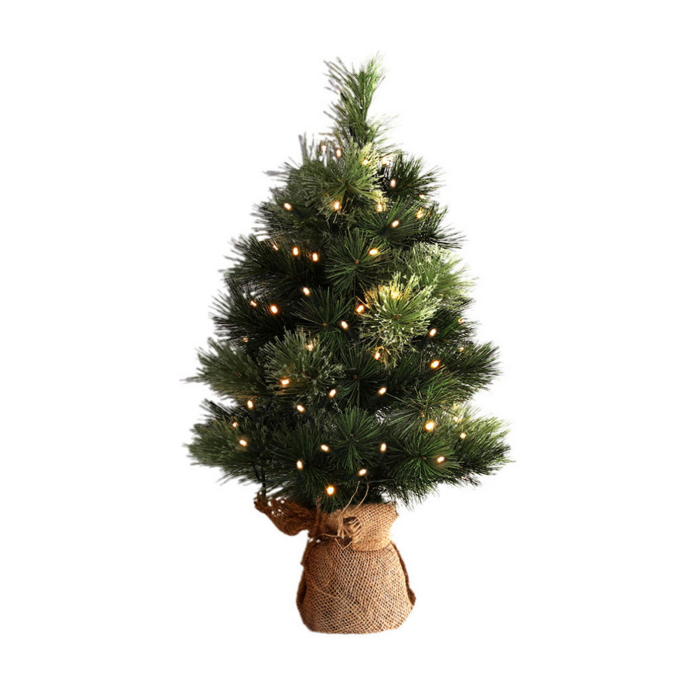 Mini tabletop Christmas tree with dark green branches and warm LED lights in a burlap bag base