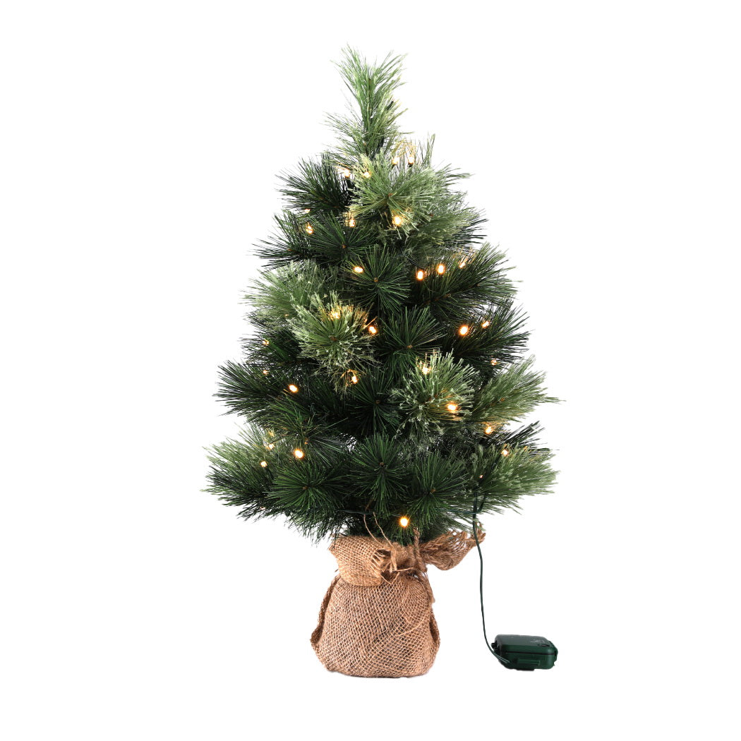 Mini tabletop Christmas tree with warm LED lights on dark green needles, burlap bag base