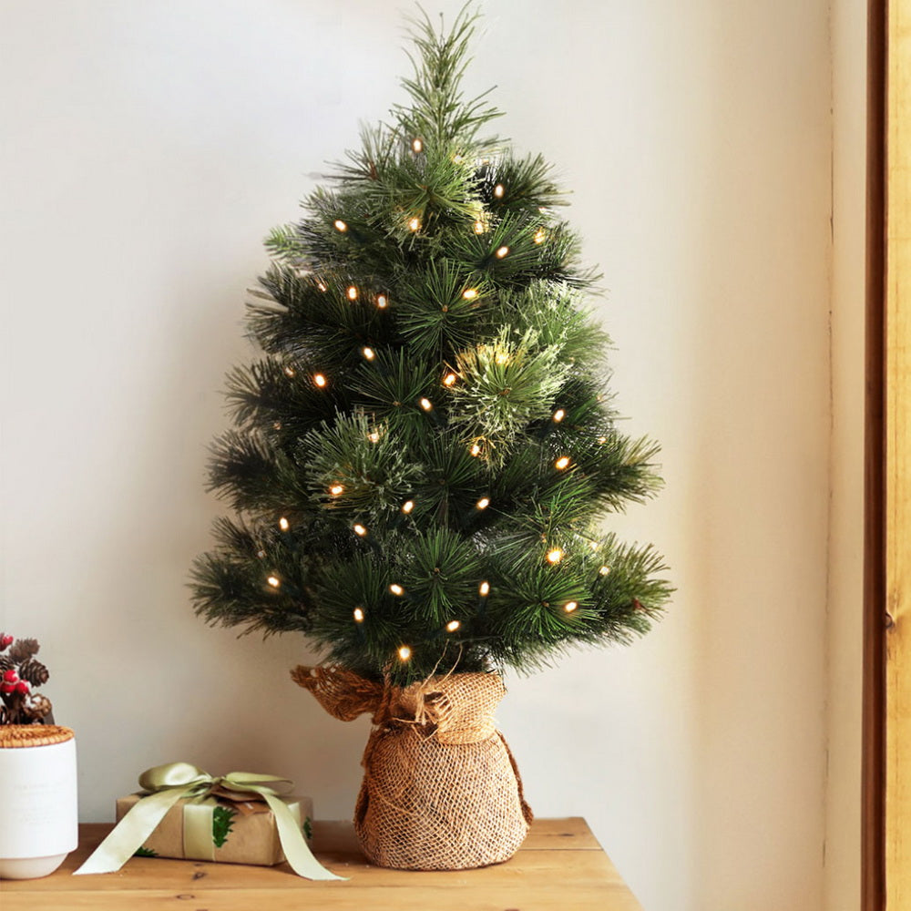 Small tabletop Christmas tree with warm LED lights and dark green branches in burlap bag base
