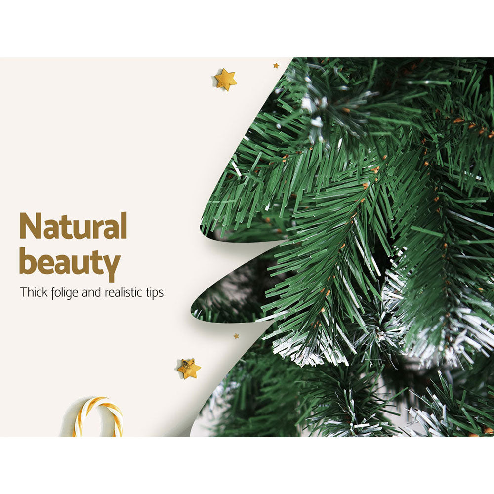 Artificial Christmas tree foliage close-up with thick green needles and white snowy tips.