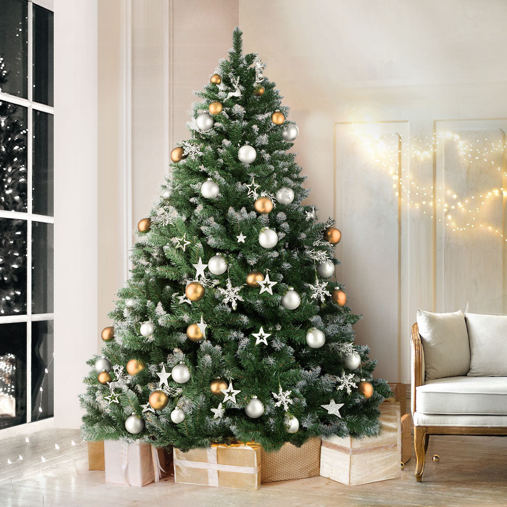 Artificial Christmas tree decorated with white baubles and gold ornaments on snowy branches.