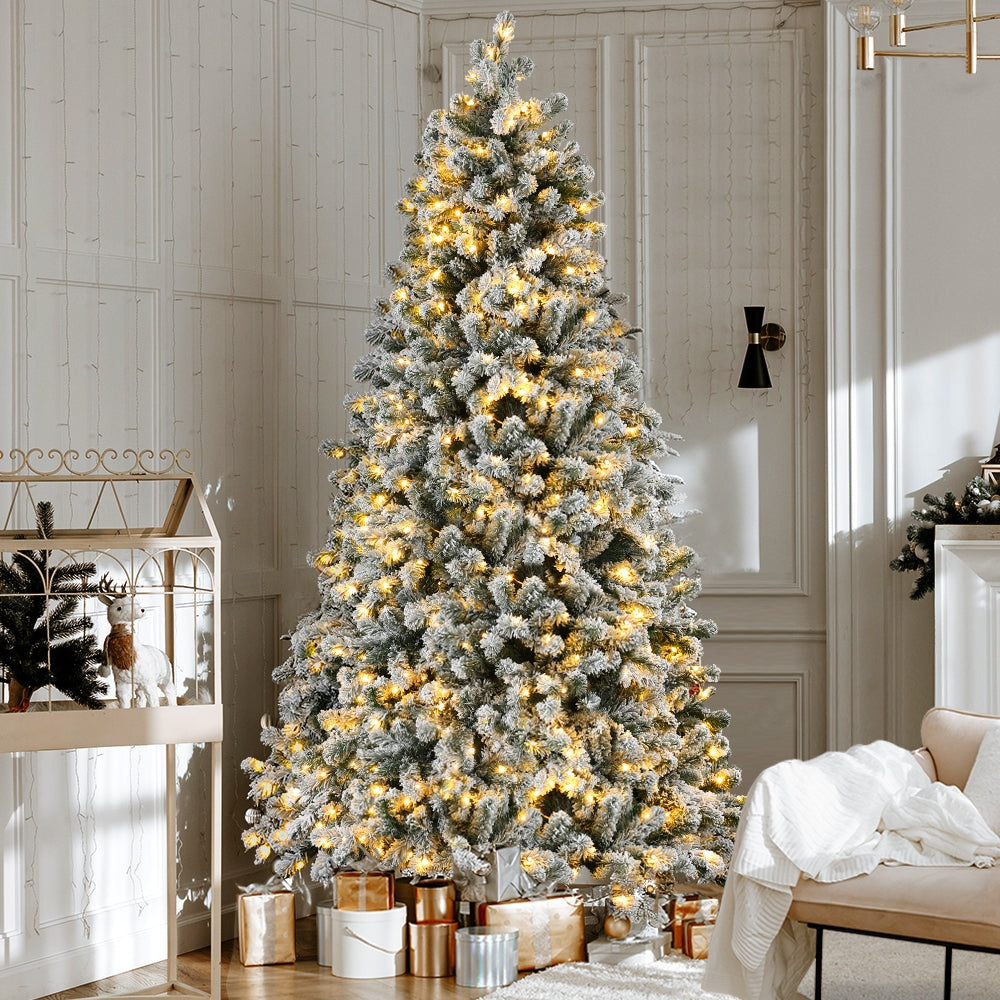 Snow-frosted Christmas tree with warm white LED lights standing upright indoors
