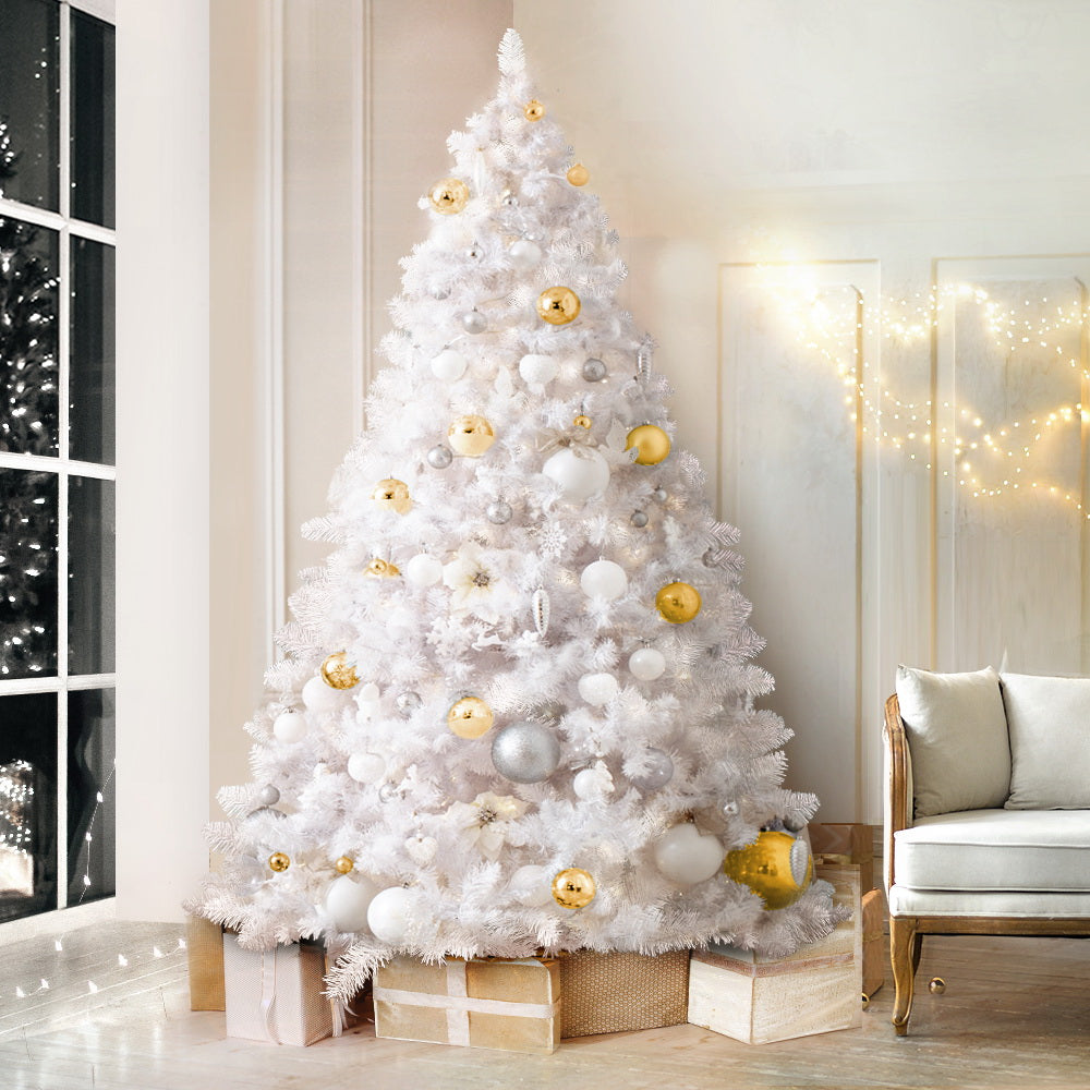 Artificial Christmas tree with white tips and gold, silver, and white ornaments near a window