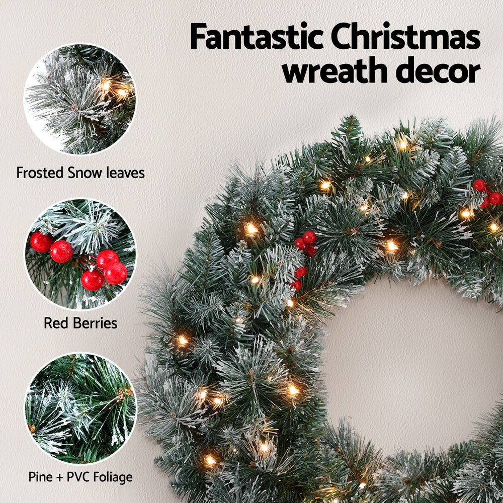 Snowy Christmas wreath with warm LED lights and red berries, frosted pine