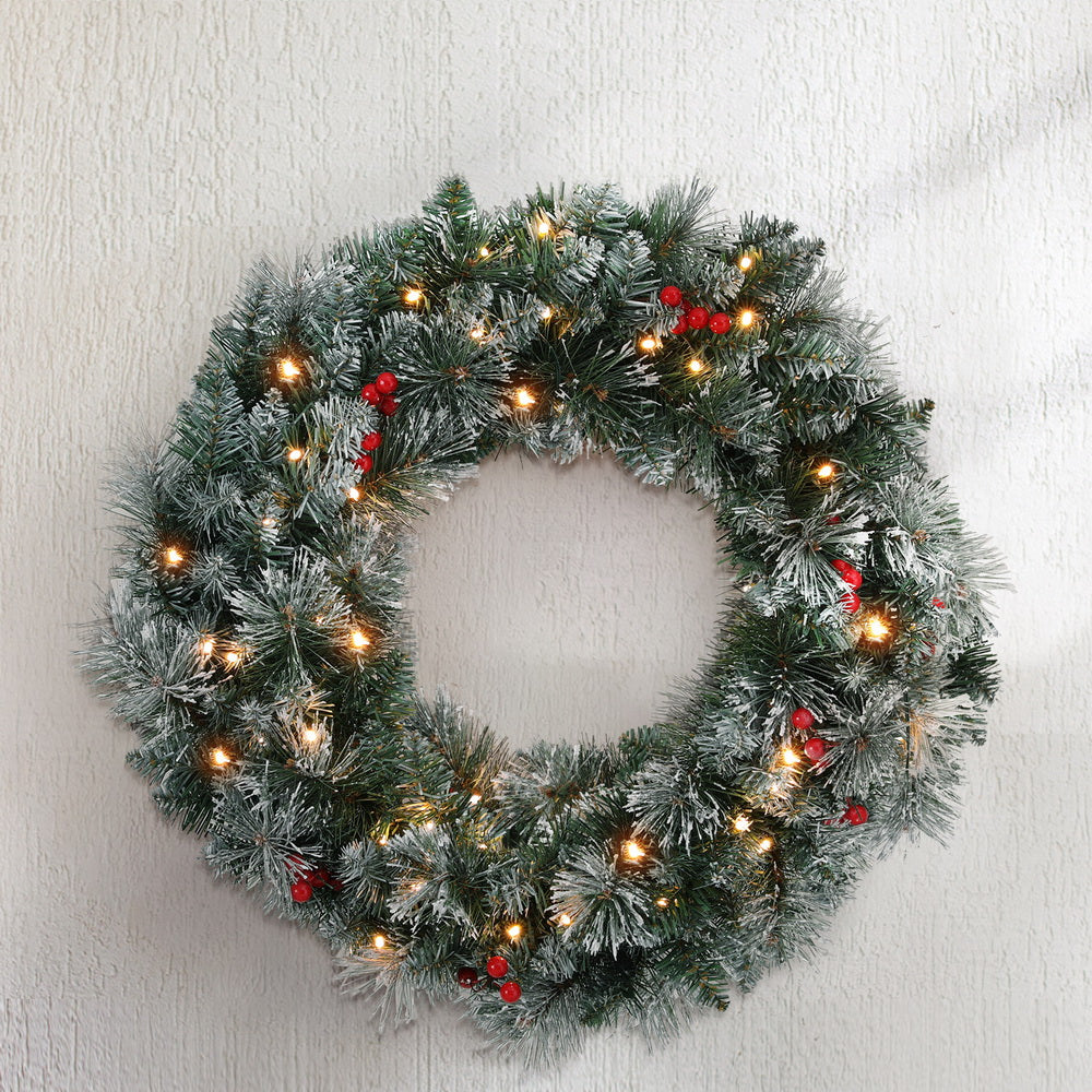 Snowy Christmas wreath with warm LED lights and red berries on a wall