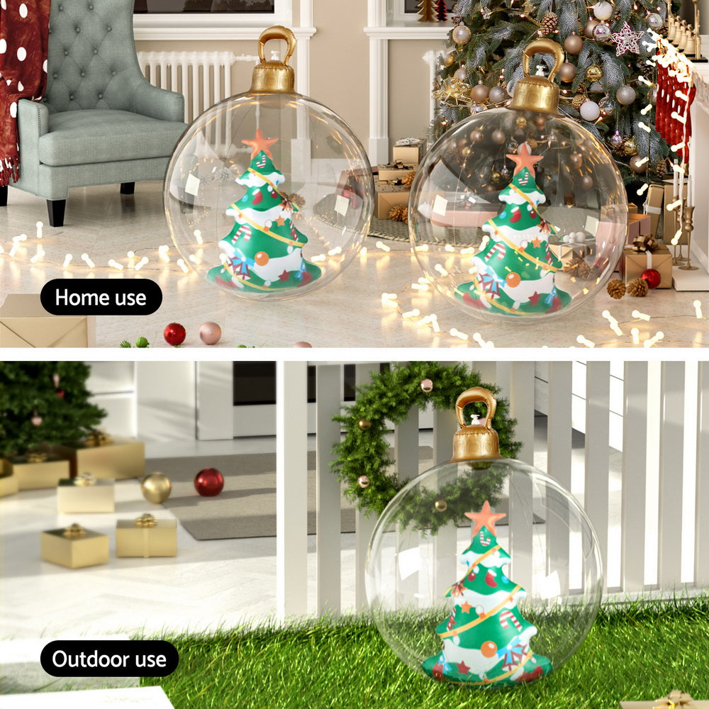 Clear inflatable Christmas bauble with gold handle and tree design, on outdoor grass