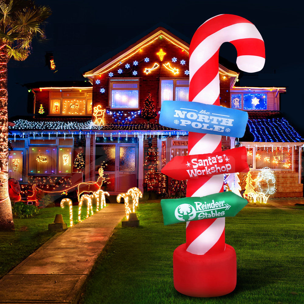 Inflatable illuminated candy cane pole decoration with lit sign panels and red base in yard.